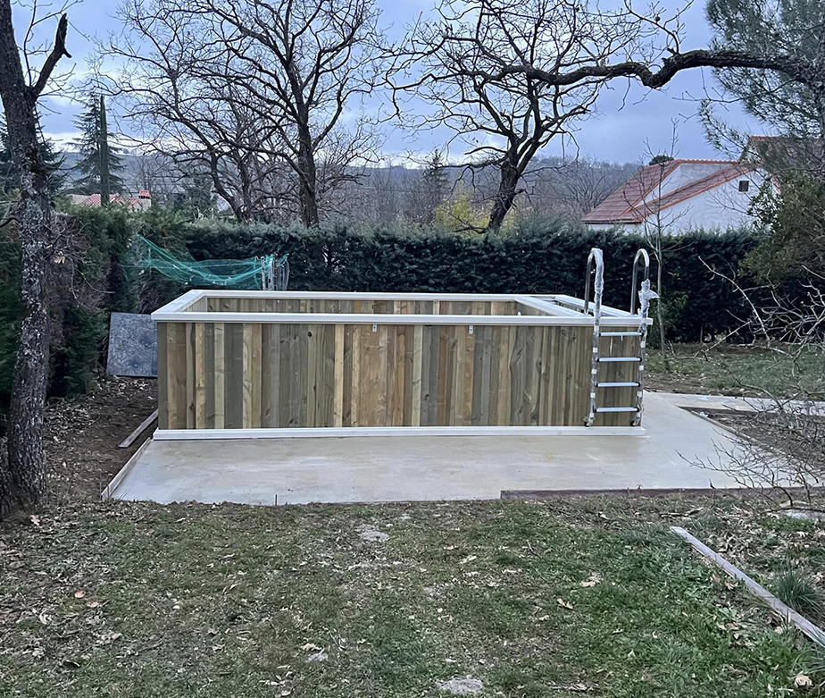 Rustic wooden above ground pool in a natural setting with bare trees and a dense hedge, ready for winter.